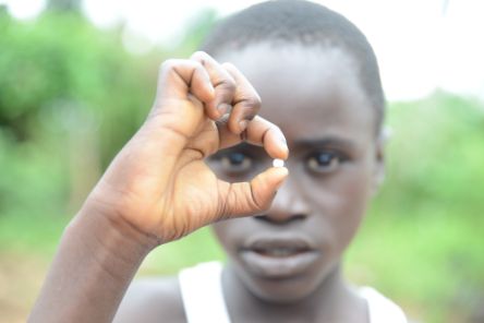 Ein afrikanisher Junge hält eine kleine Tablette zwischen den Fingern und hält sie vor sein Gesicht.