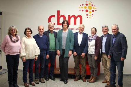 Eine Gruppe von neun Personen steht vor einer Wand mit dem rot-gelben CBM-Logo.