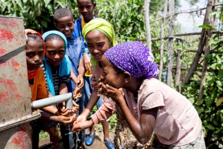 Afrikanische Schüler*innen waschen sich an einer Wasserpumpe das Gesicht