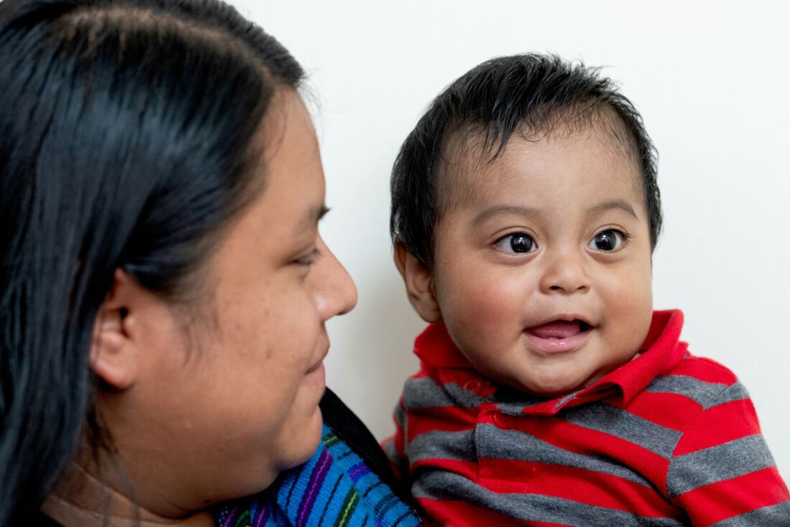 Eine Frau hält ein etwa neun Monate altes Baby auf dem Arm. Das Baby lächelt.