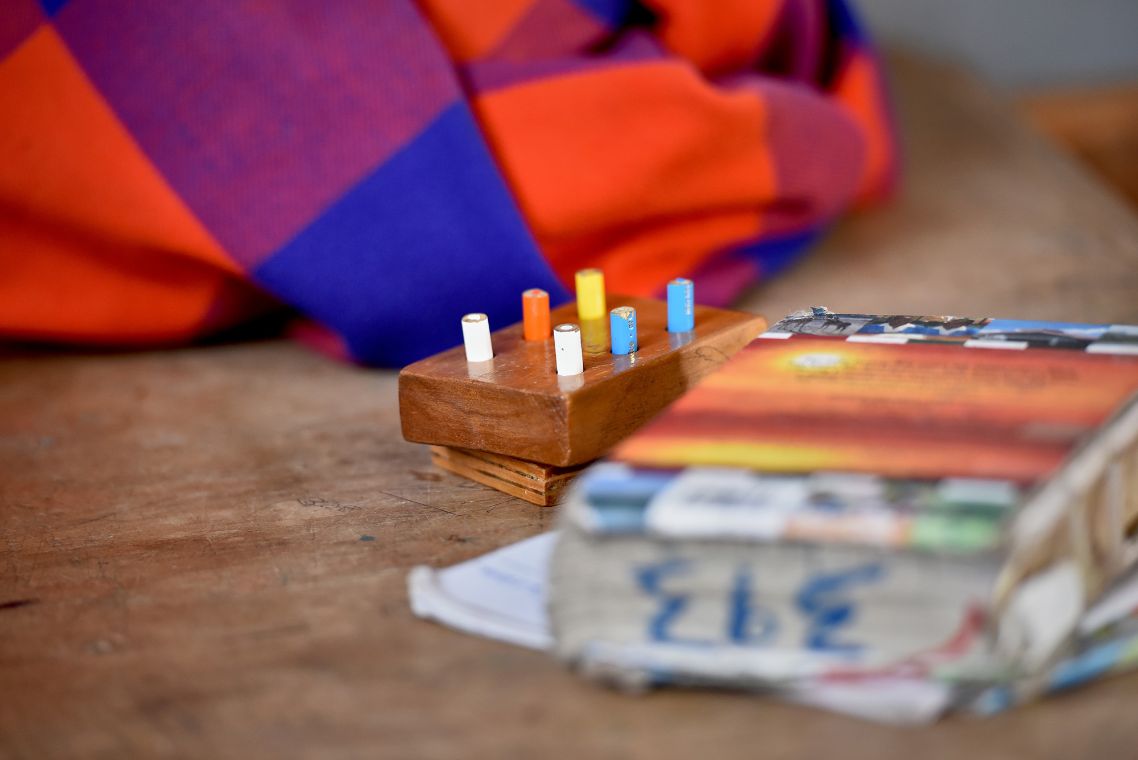 neben einem Buch liegt ein Holzstück mit sechs Löchern, in denen Buntstifte stecken