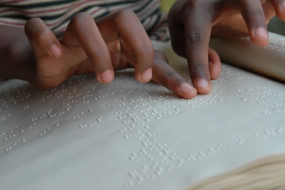 Zwei Hände fahren über ein Blatt Papier mit Braille.