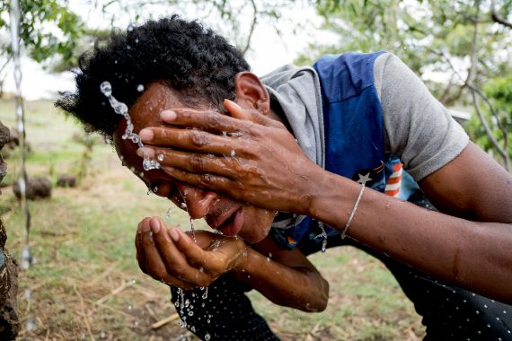 Ein junger Mann beugt sich unter einen Wasserstrahl und wäscht sich das Gesicht.