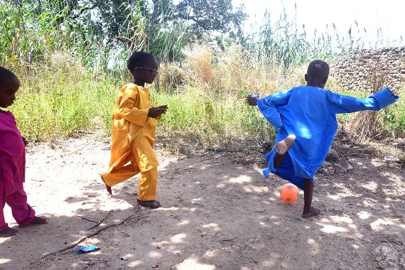 Drei kleine Jungen in bunten Kaftanen spielen Fußball.